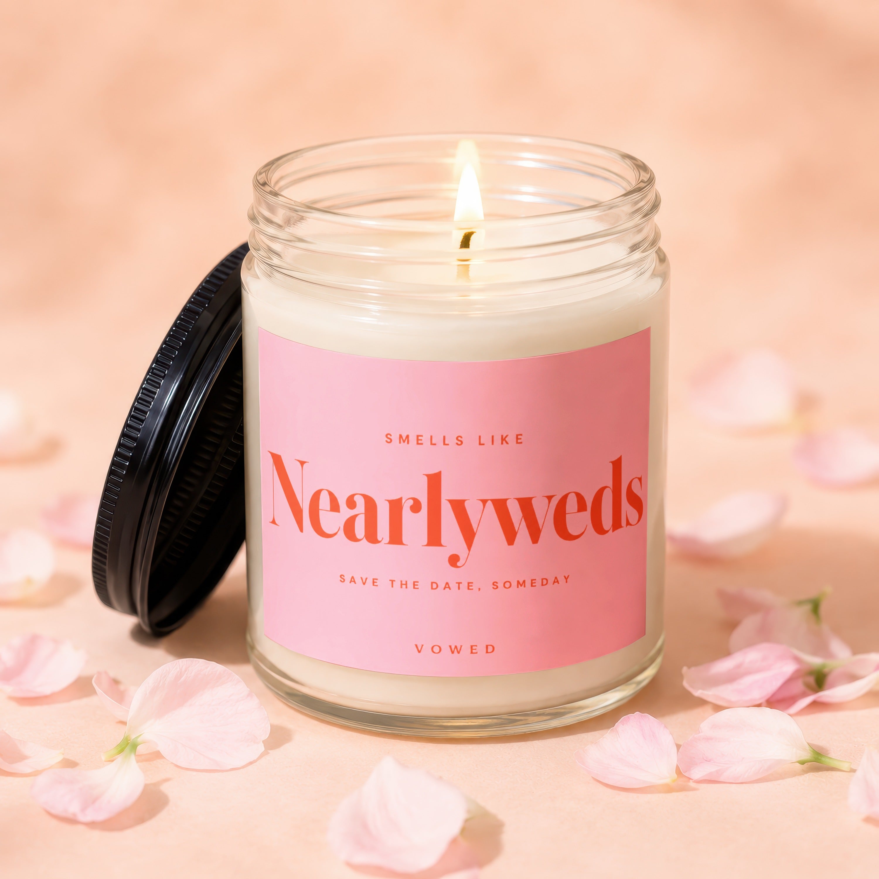 Glass candle with pink label saying "Smells Like Nearlyweds" surrounded by petals.