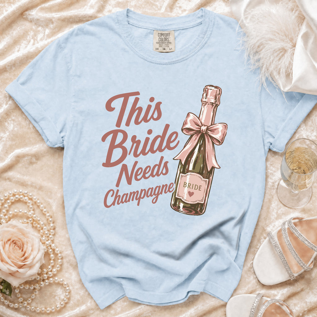 Light blue t-shirt with "This Bride Needs Champagne" text and champagne bottle graphic.