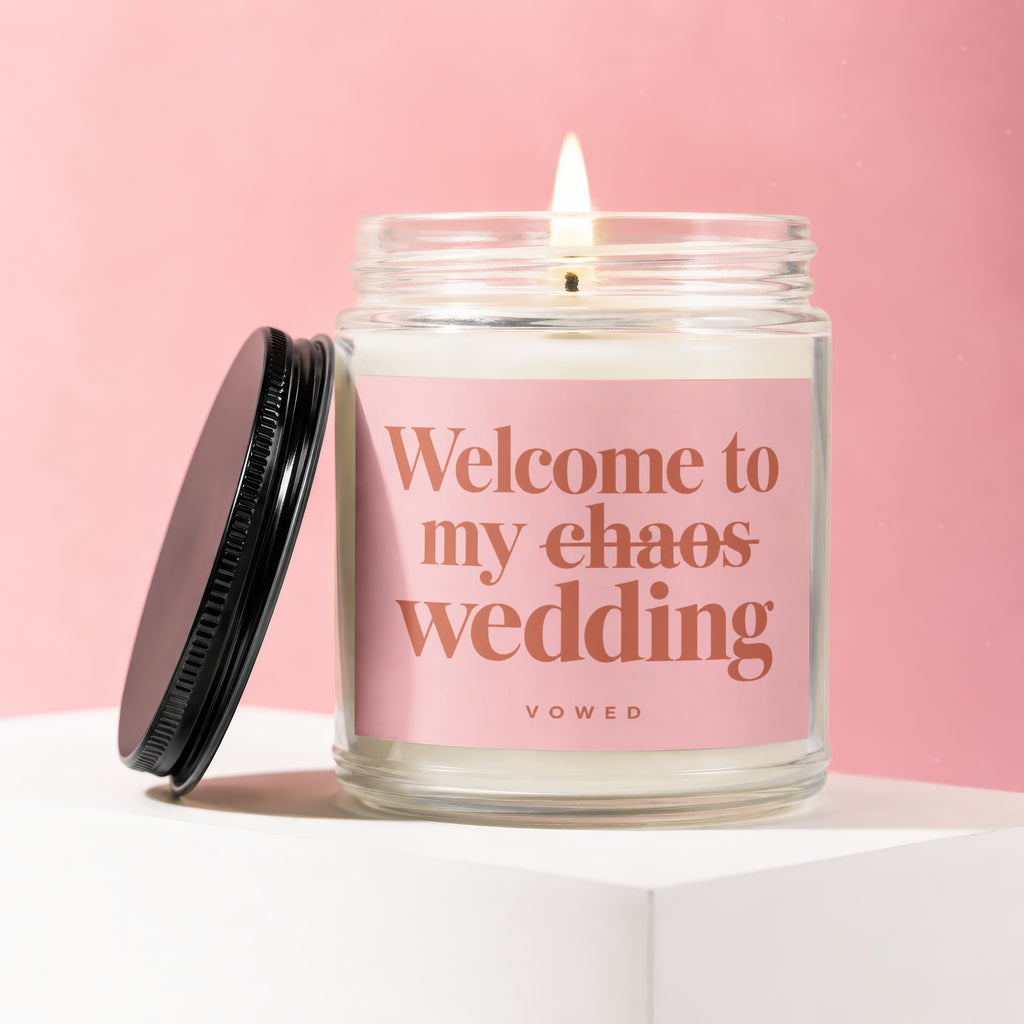 Lit candle in a glass jar with a pink label that reads "Welcome to my chaos wedding".
