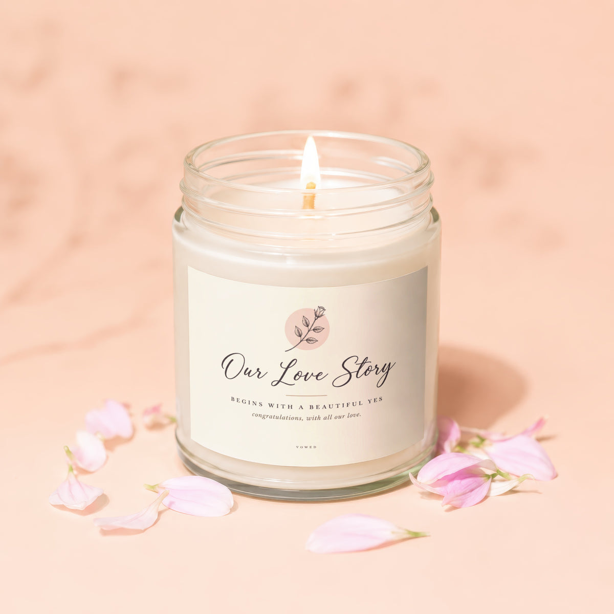 Burning candle in glass jar labeled "Our Love Story" with flower graphic.
