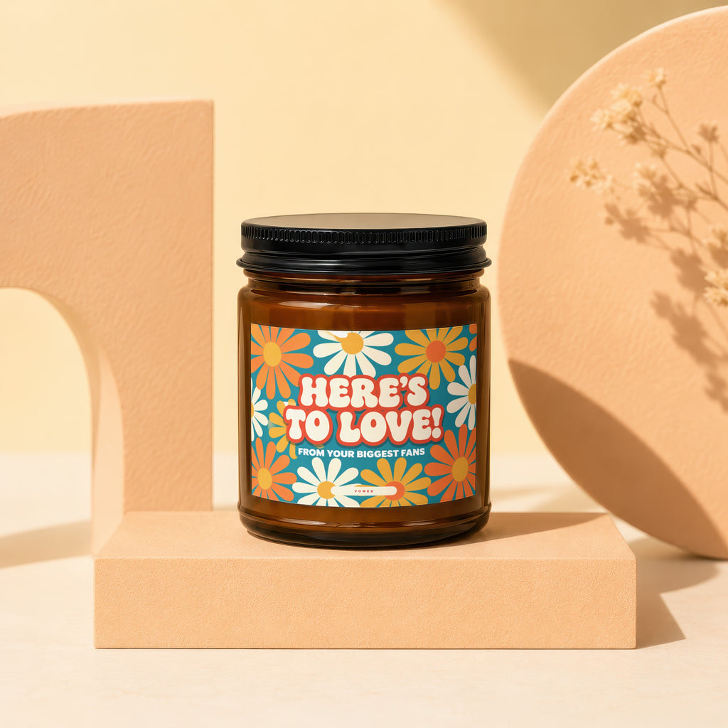 Amber candle with a retro daisy label reading "HERE'S TO LOVE! FROM YOUR BIGGEST FANS".