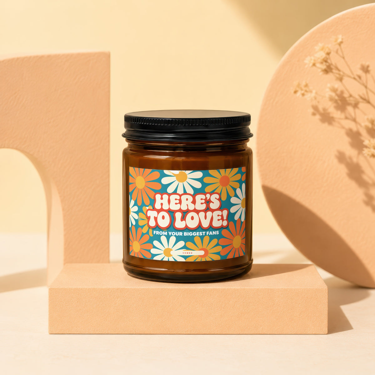 Amber candle with a retro daisy label reading "HERE'S TO LOVE! FROM YOUR BIGGEST FANS".