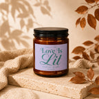 Amber candle with a black lid on a textured stone, labeled "Love Is Lit".