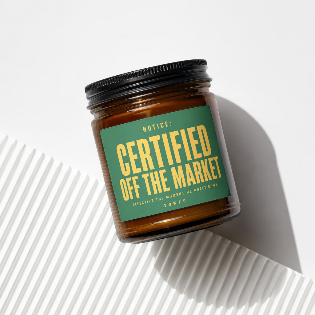 Amber candle in glass jar with black lid and green label saying "Certified Off the Market."