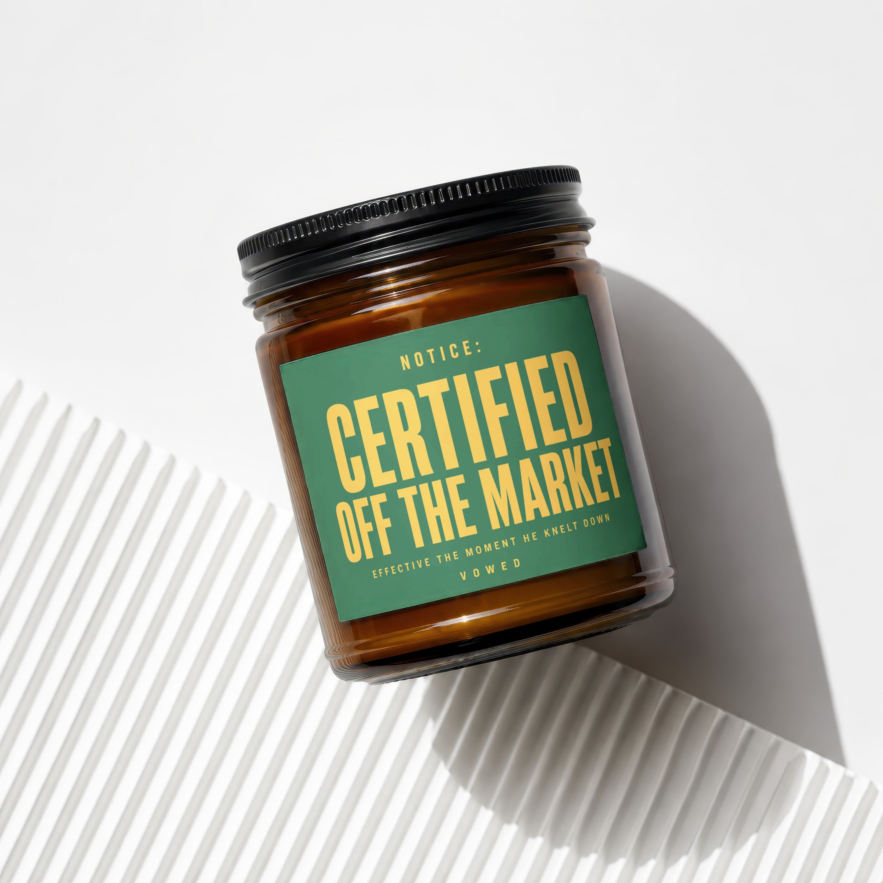 Amber candle in glass jar with black lid and green label saying "Certified Off the Market."