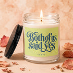 Lit candle in glass jar with "Both of us said yes" and "VOWED" text on label.
