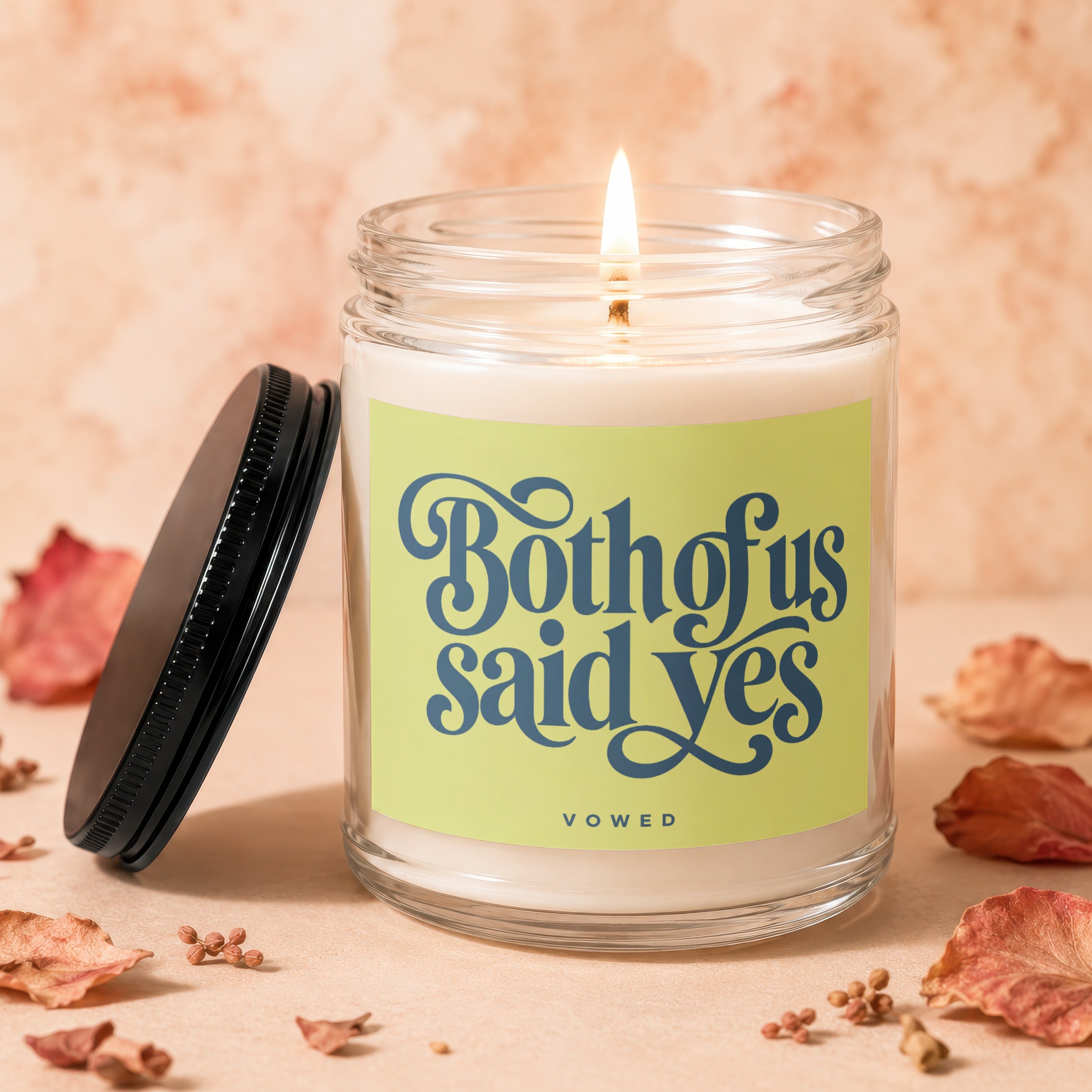 Lit candle in glass jar with "Both of us said yes" and "VOWED" text on label.