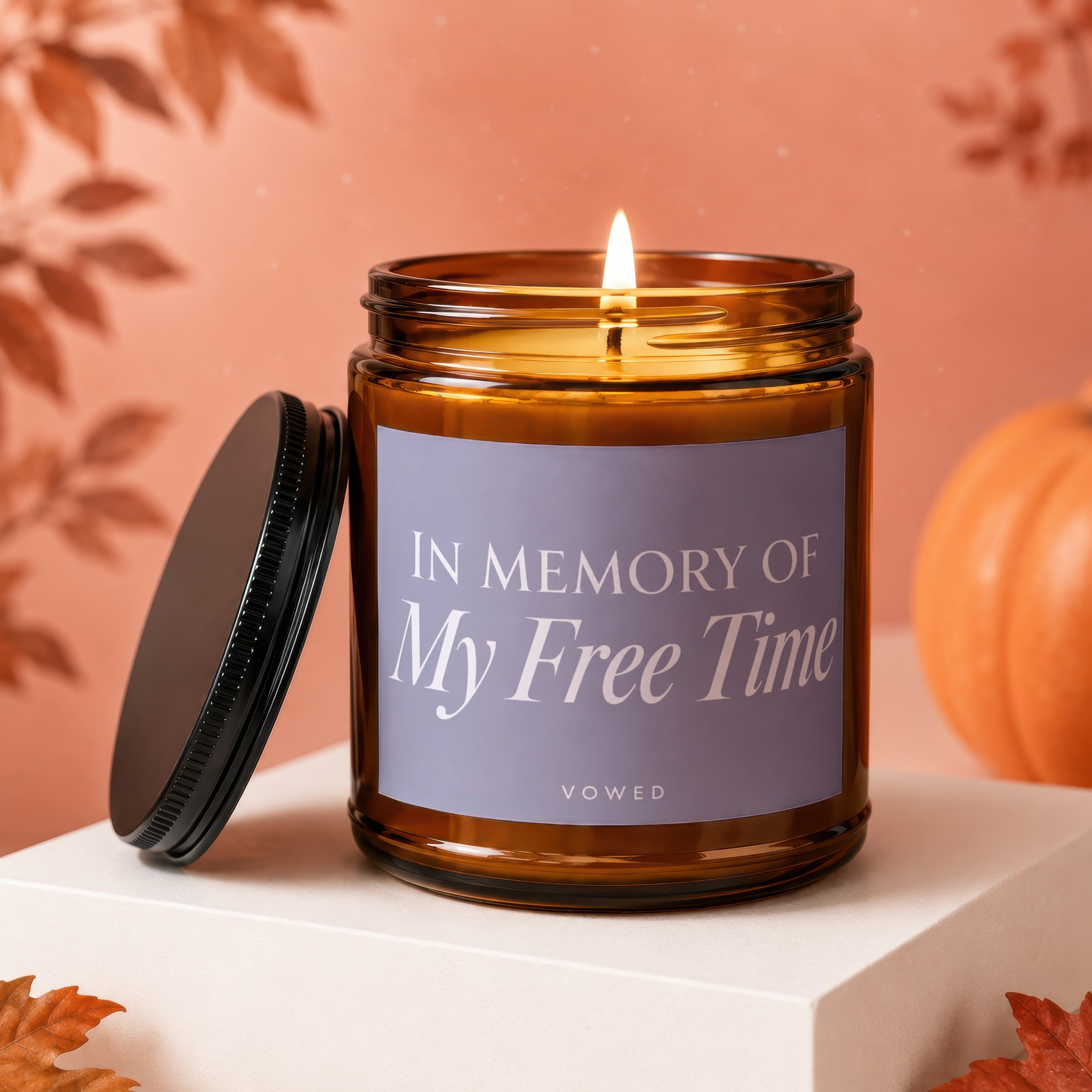 Amber jar candle with lit wick reading "In Memory of My Free Time"