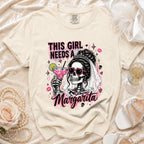Cream graphic tee with skeleton bride holding margarita and text THIS GIRL NEEDS A MARGARITA.