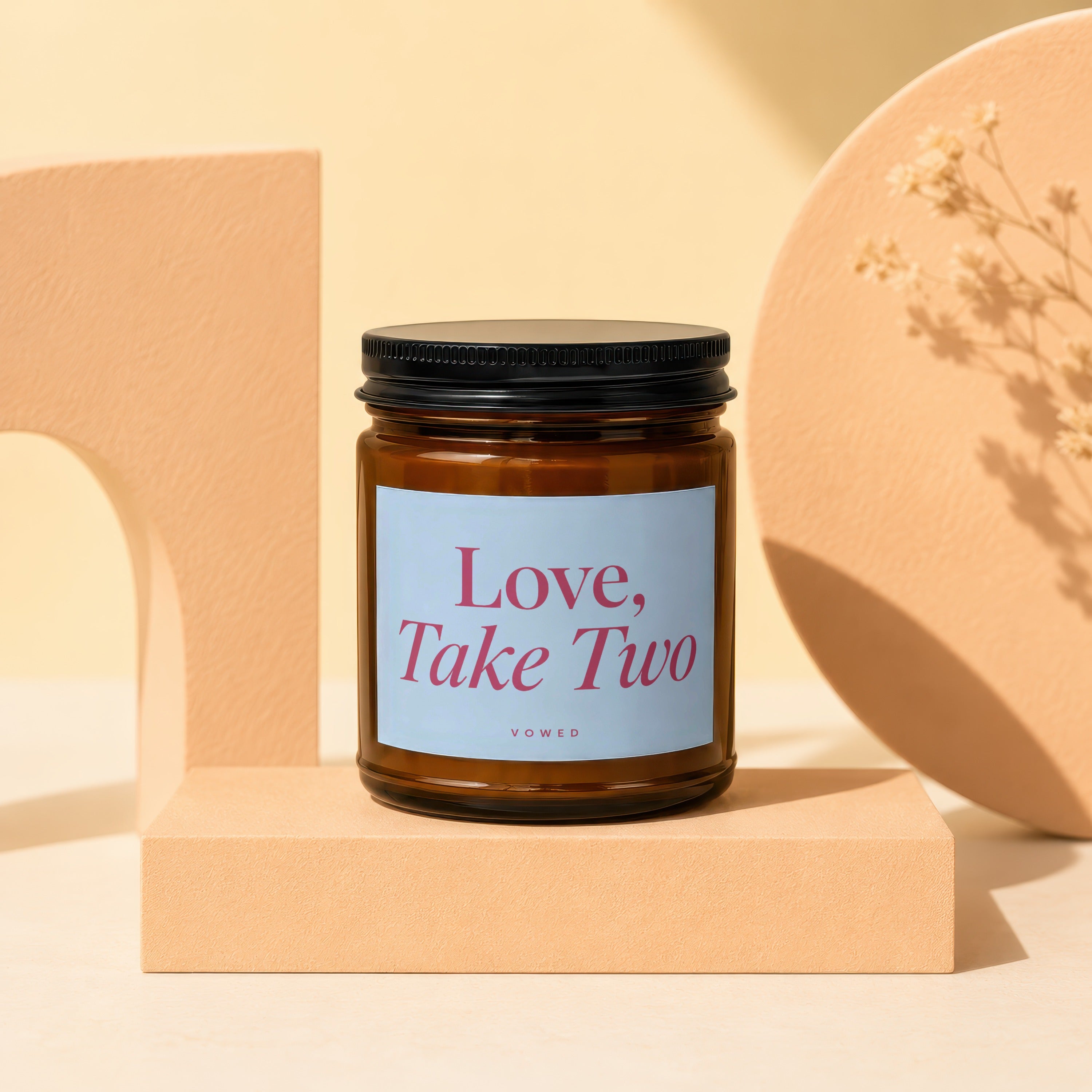 Candle with "Love, Take Two" text on a light blue label, on a display stand.