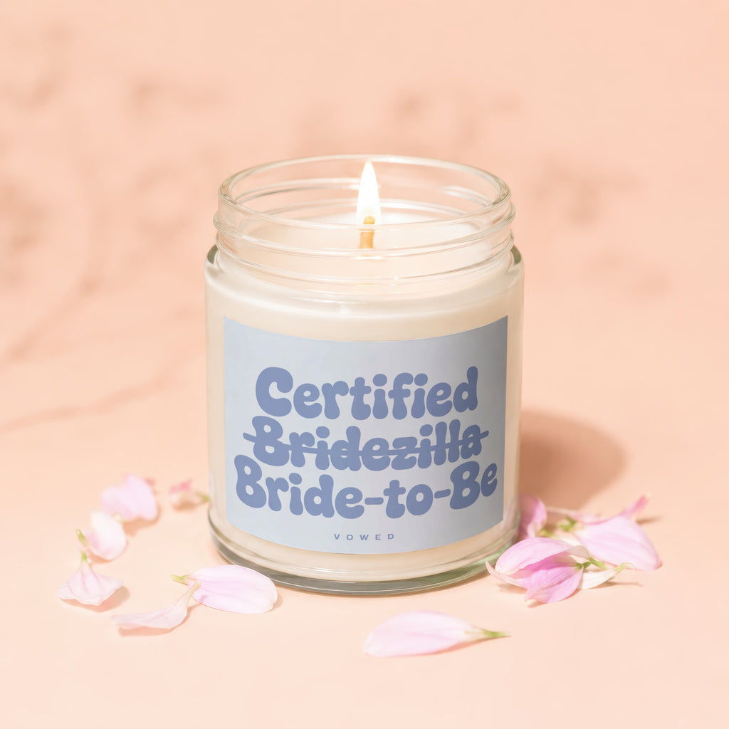 Lit candle in glass jar with "Certified Bridezilla Bride-to-Be" label and pink petals.