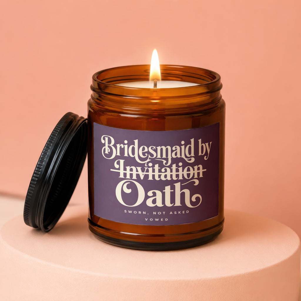 Amber jar candle with lit wick and lid off, reads "Bridesmaid by Invitation Oath".
