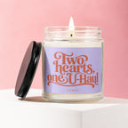 Candle with a lit wick and a purple label that reads "Two hearts, one U-Haul".