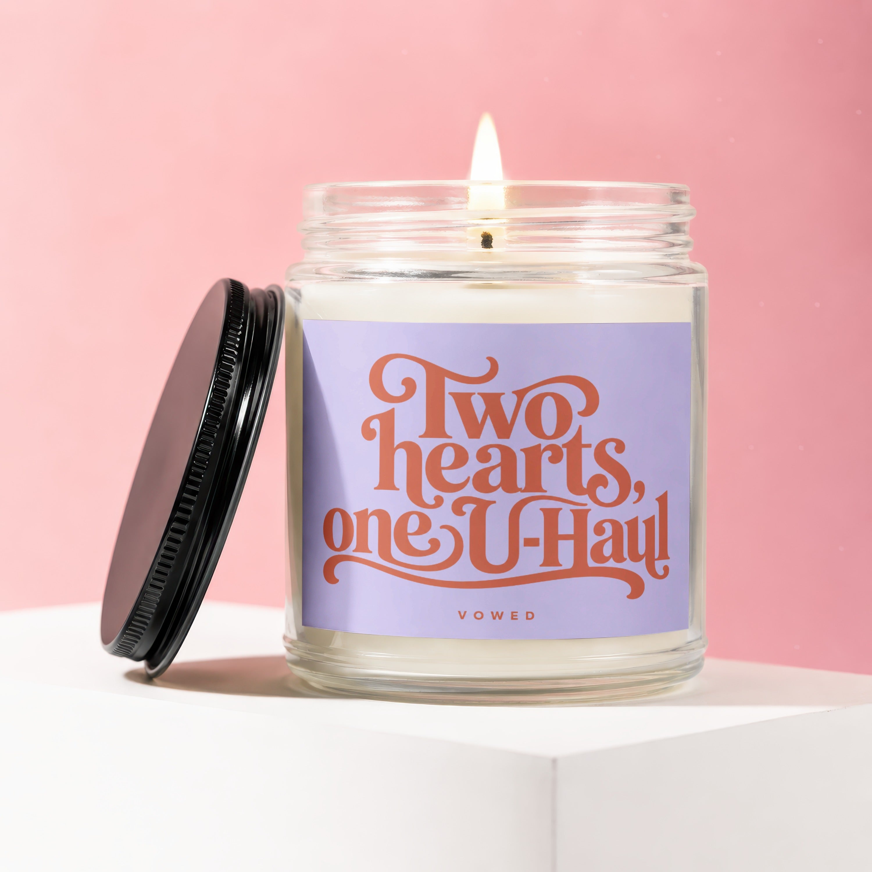 Candle with a lit wick and a purple label that reads "Two hearts, one U-Haul".