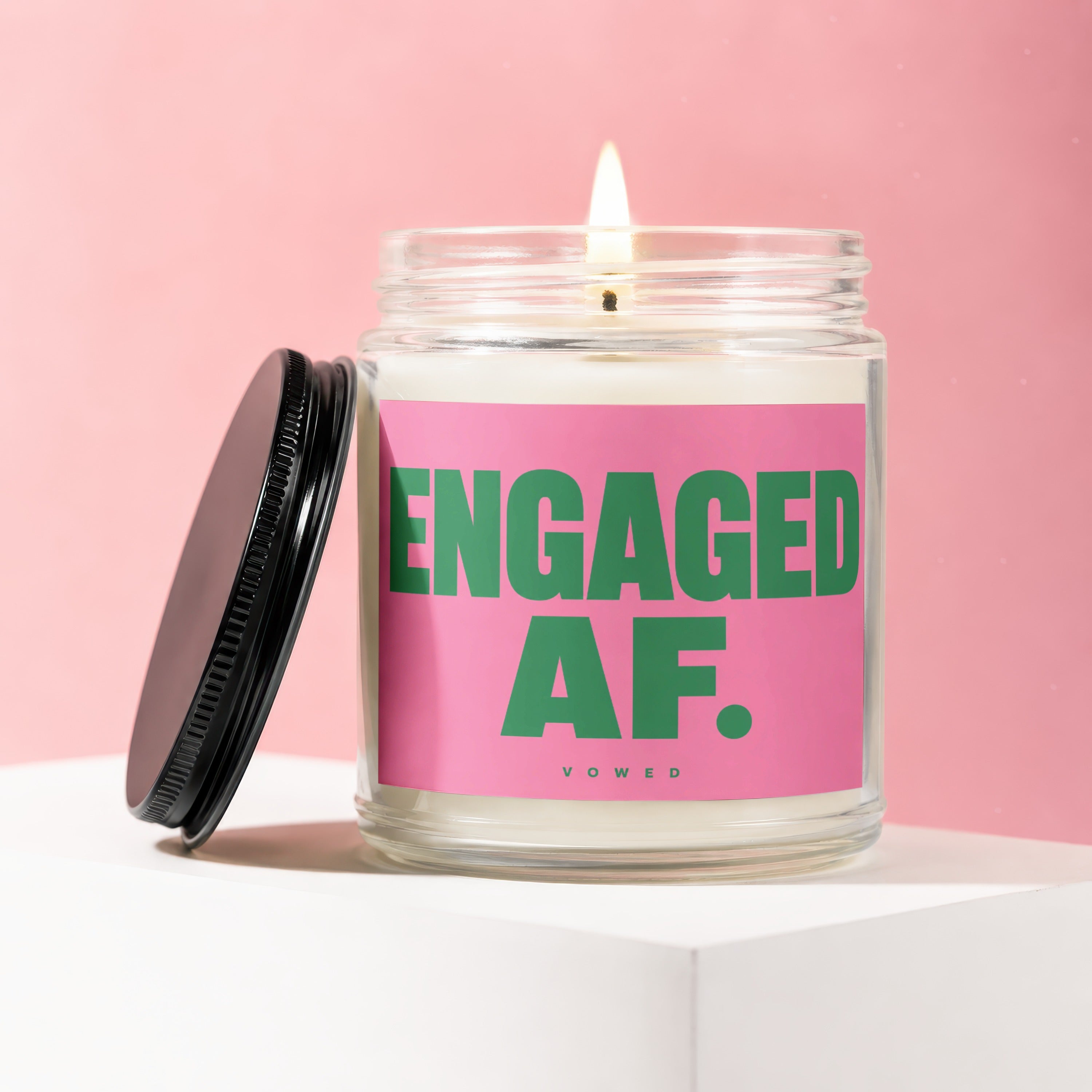 Clear jar candle with lit wick and black lid, featuring a pink label with "ENGAGED AF." text.