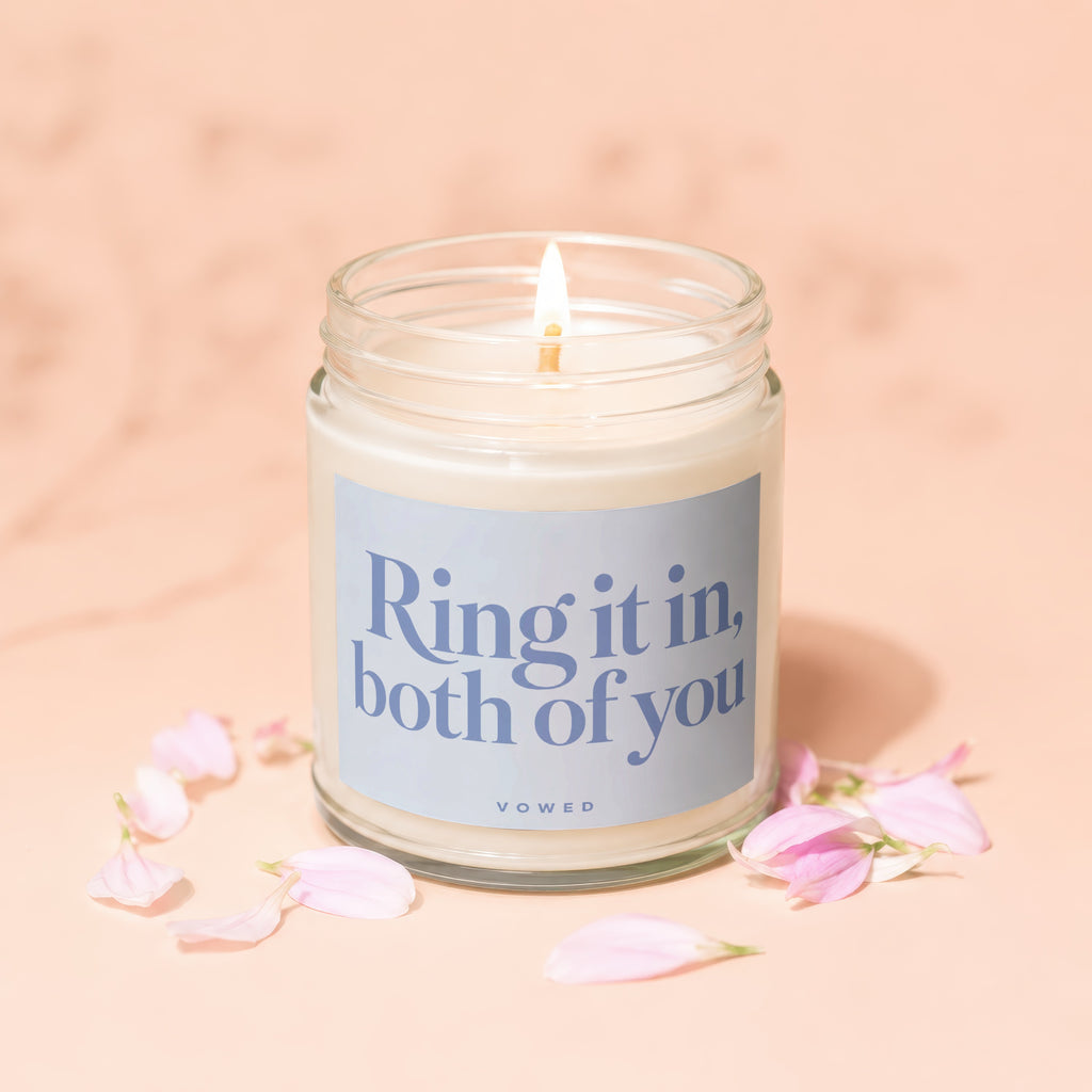 Lit candle in a glass jar with blue label saying "Ring it in, both of you".