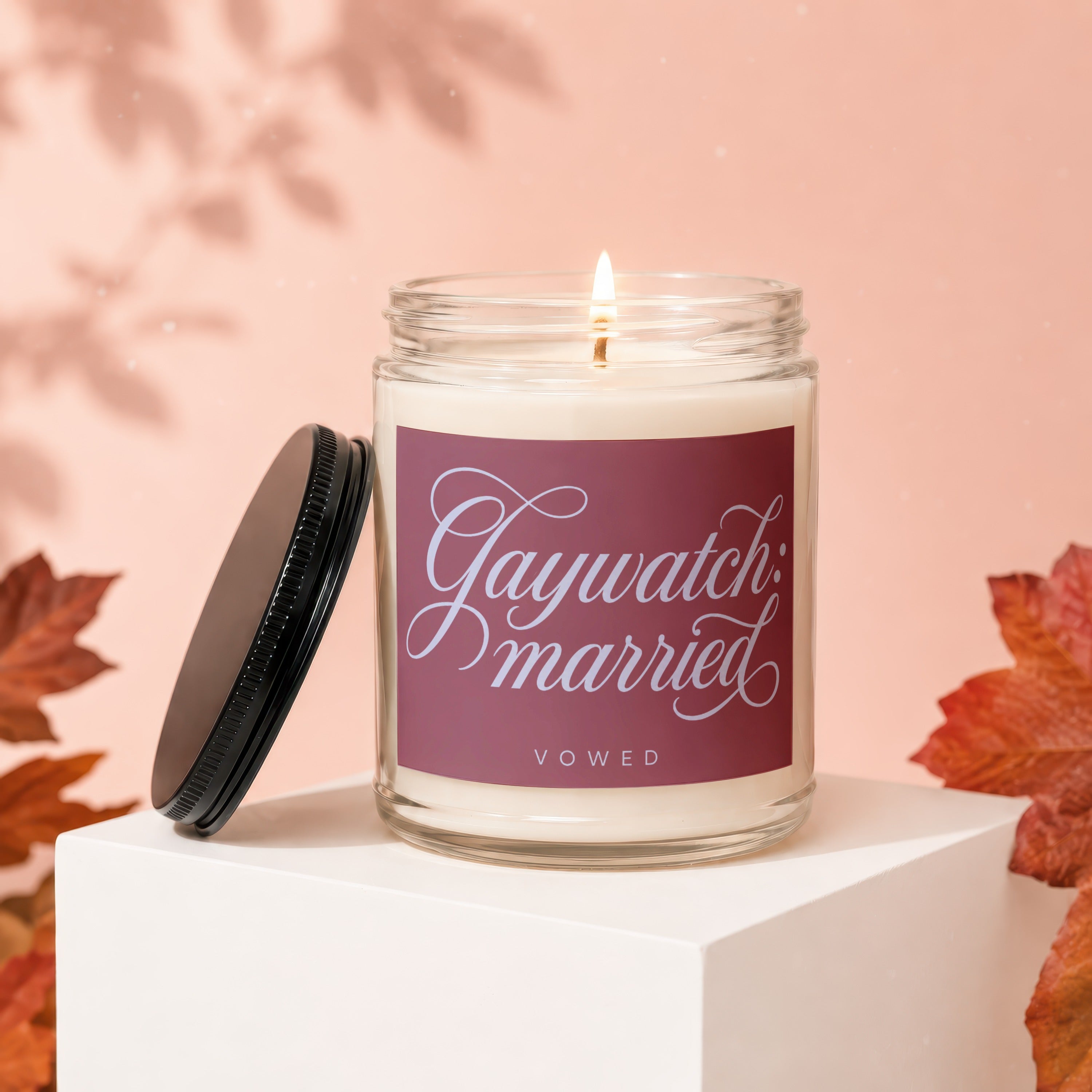 Glass candle with lit wick, labeled "Gaywatch: married", with lid off.