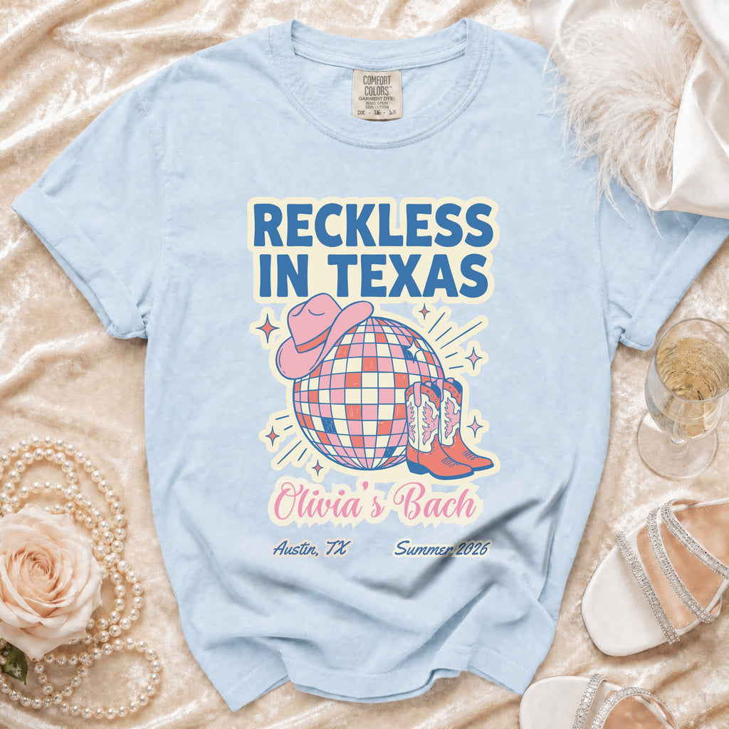 Light blue t-shirt with "Reckless In Texas" text, disco ball, cowboy boots, and hat.