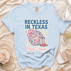 Light blue t-shirt with "Reckless In Texas" text, disco ball, cowboy boots, and hat.