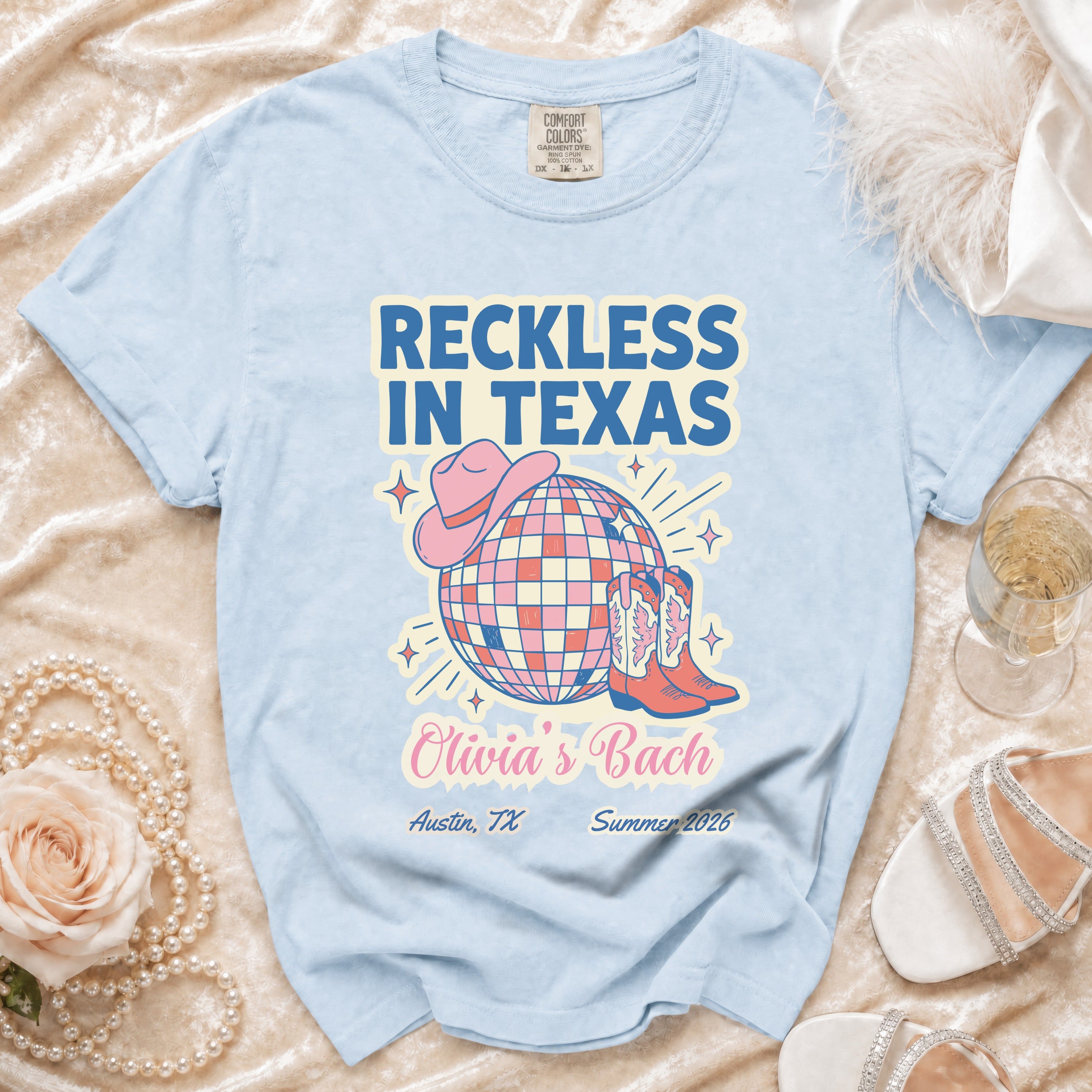 Light blue t-shirt with "Reckless In Texas" text, disco ball, cowboy boots, and hat.