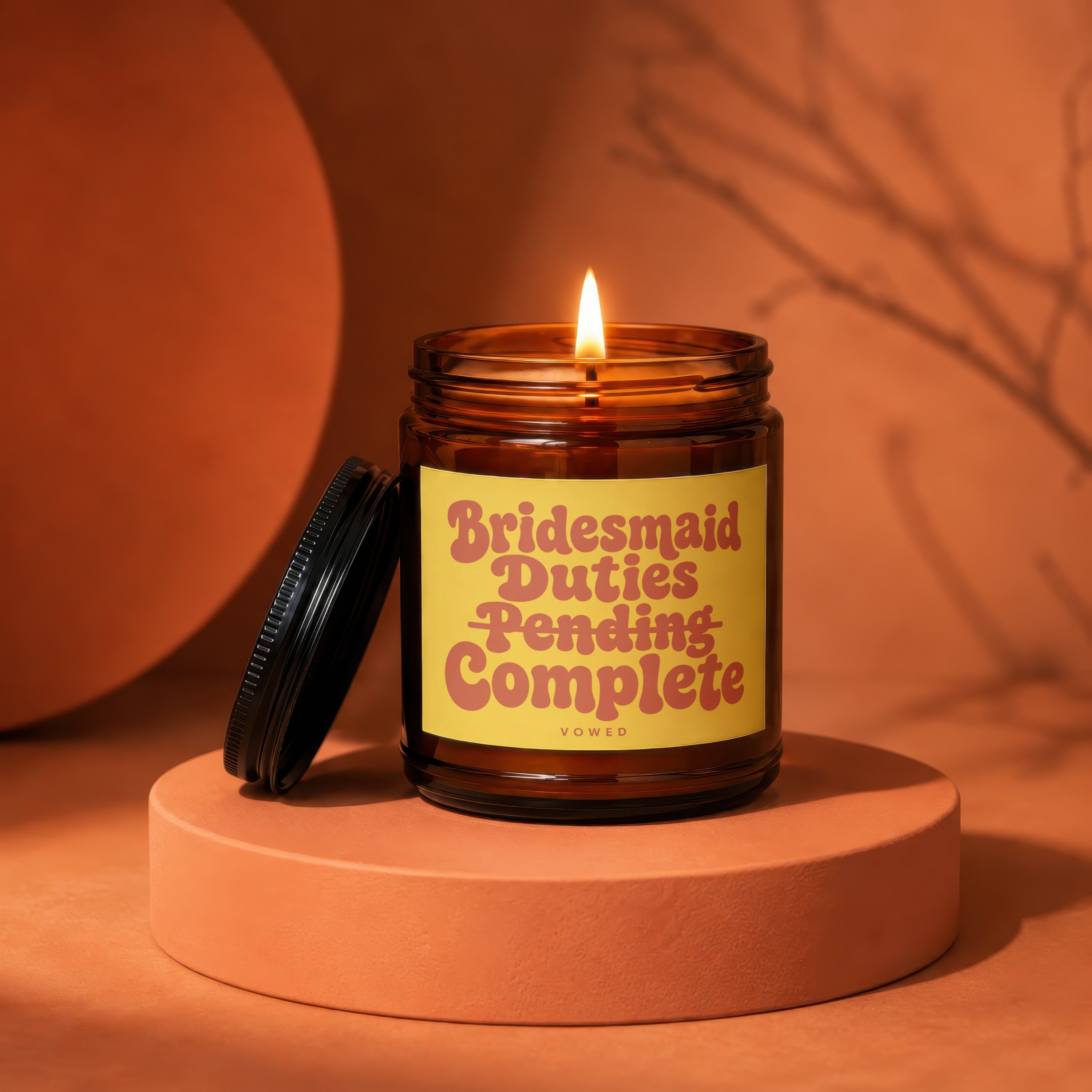 Amber jar candle with lit flame and yellow label reading "Bridesmaid Duties Pending Complete".