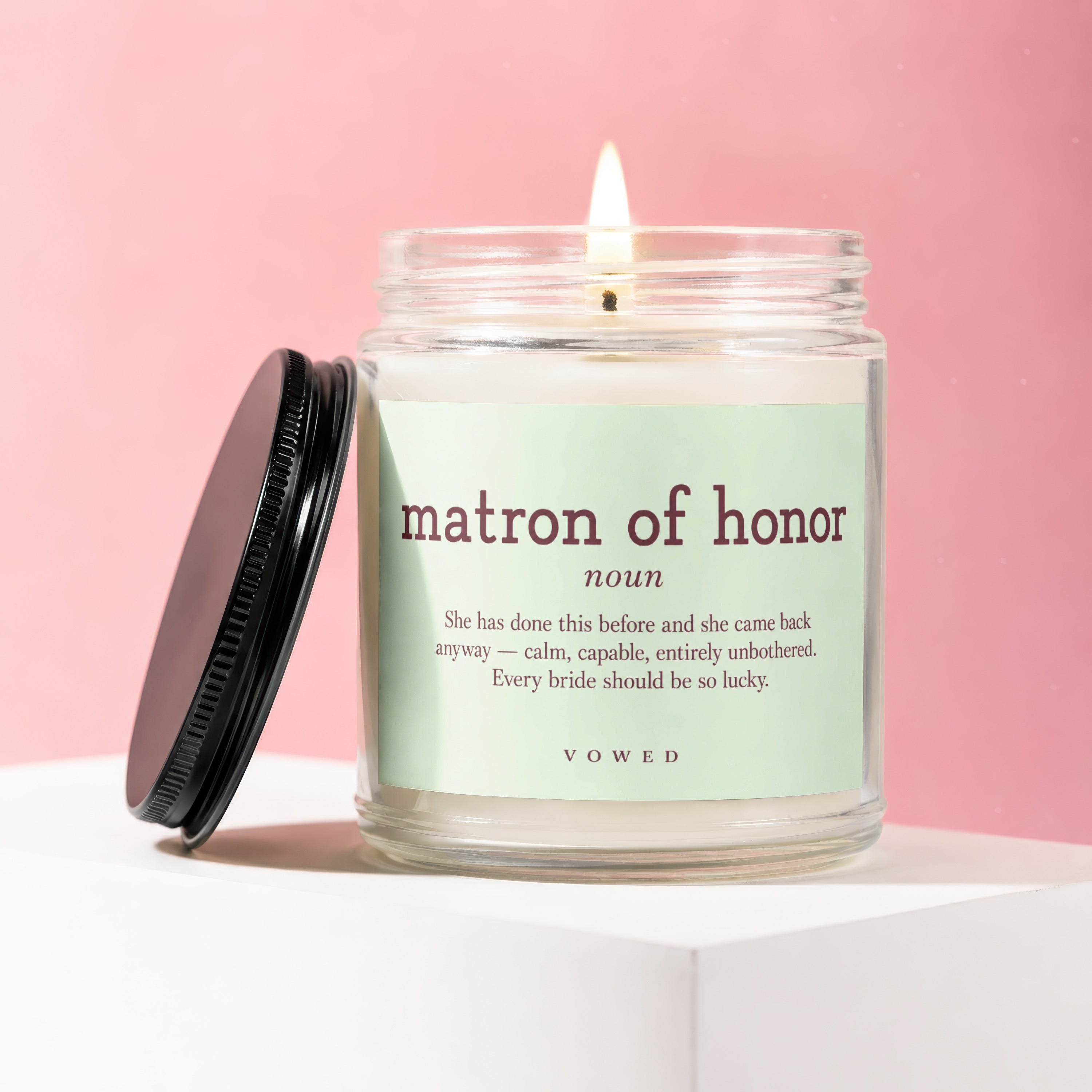 Candle with "matron of honor" definition and "VOWED" branding on a pink background.