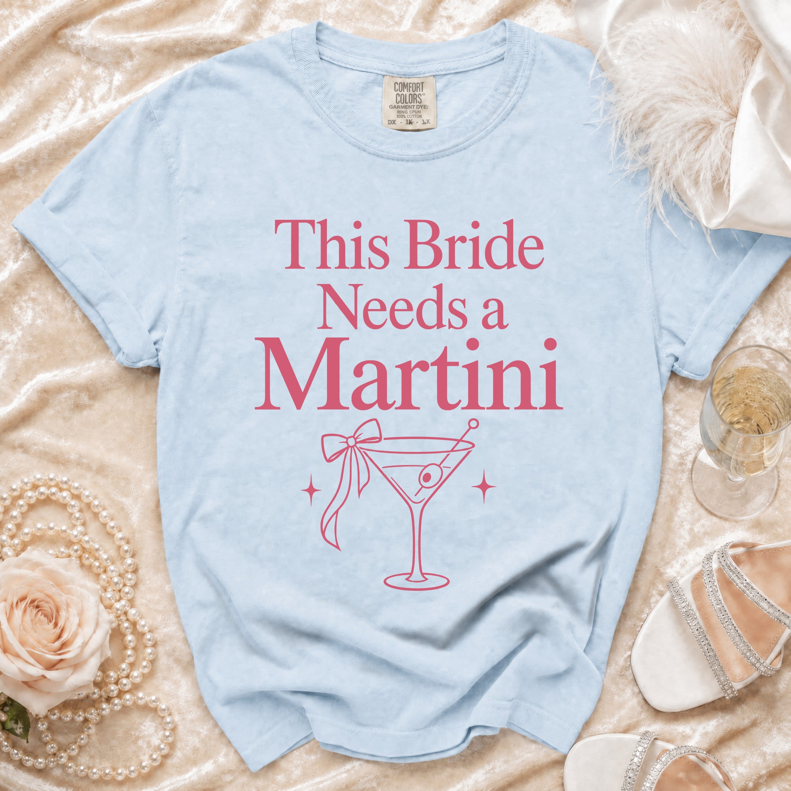 Light blue t-shirt with pink text "This Bride Needs a Martini" and martini glass graphic.