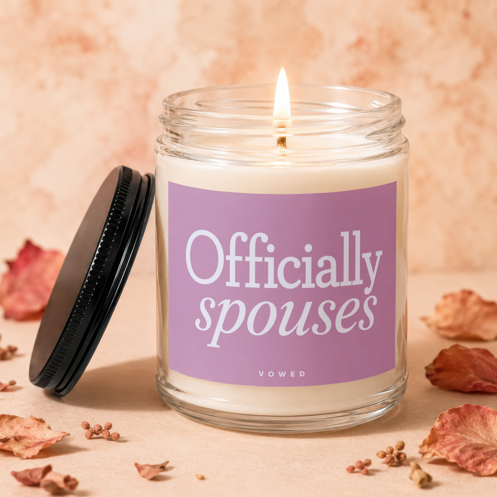 Glass candle with lit wick and purple label reading "Officially spouses"
