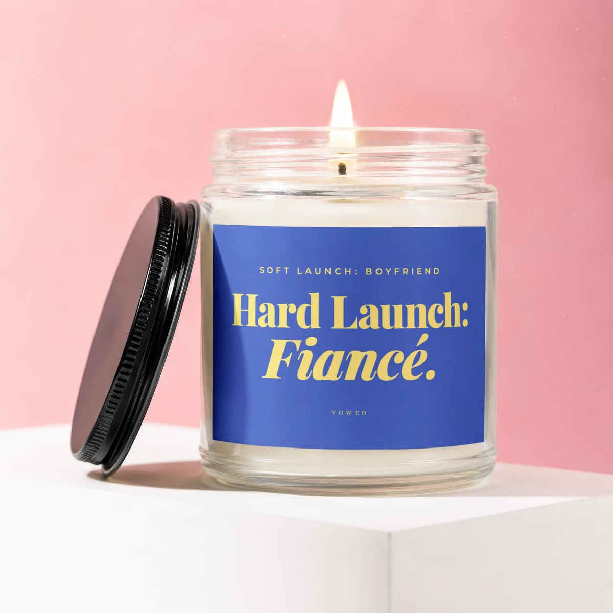 Lit candle in glass jar with blue label that reads "Hard Launch: Fiancé."