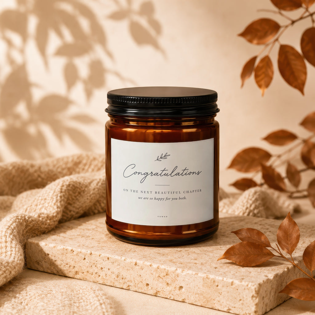 Amber candle with black lid, "Congratulations" text, on beige textured surface with fabric.