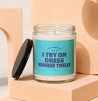 Glass candle with teal label reading "I Try On Dress Number Twelve".