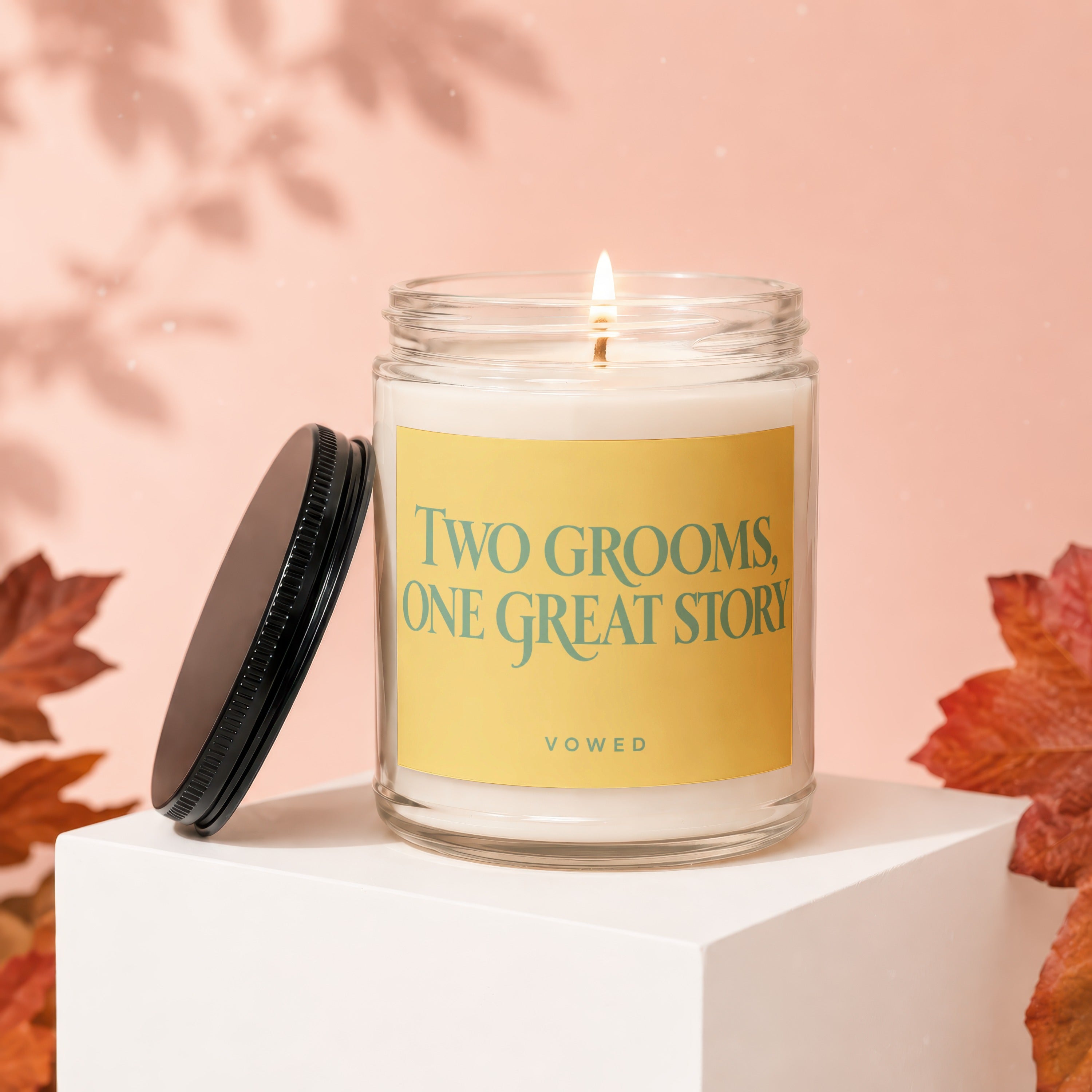 Candle with lit flame and text "Two Grooms, One Great Story" on yellow label.