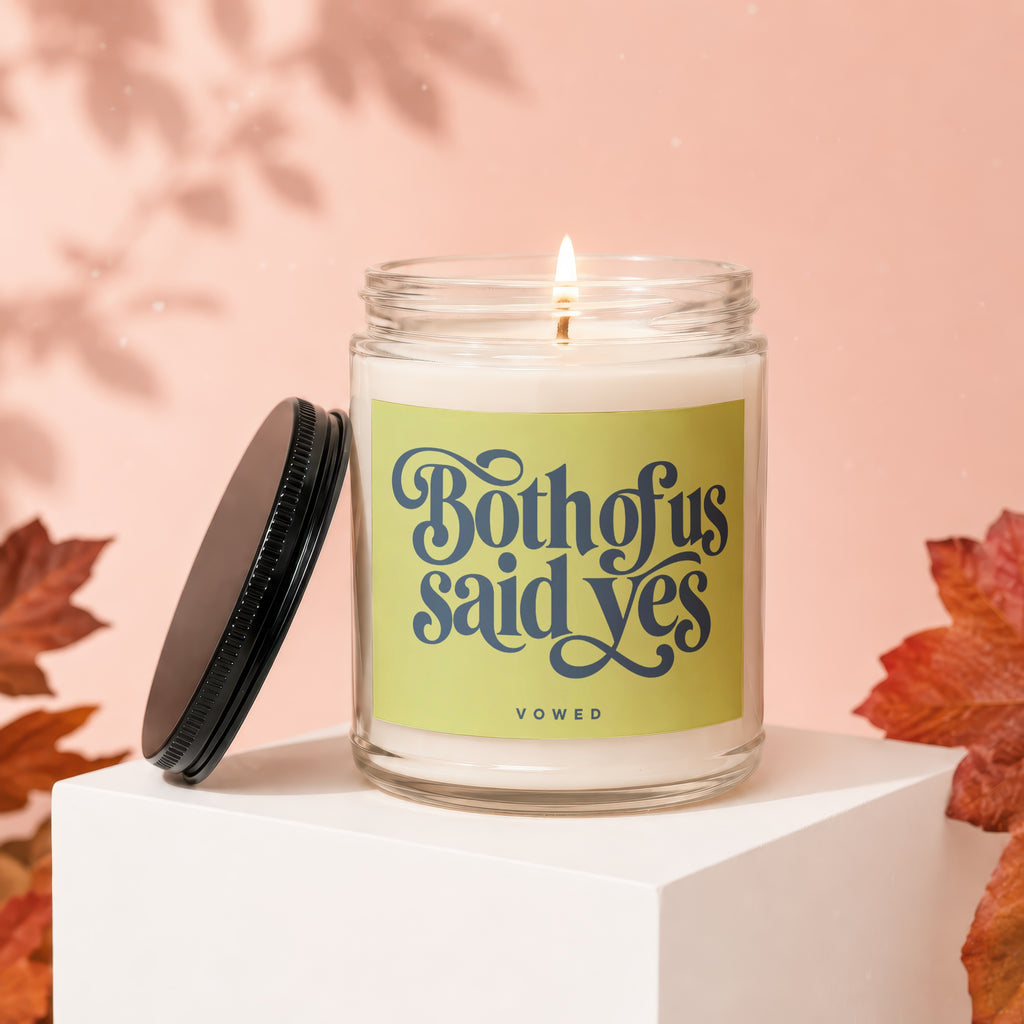 Lit candle in glass jar with "Both of us said yes" text and "VOWED" label.