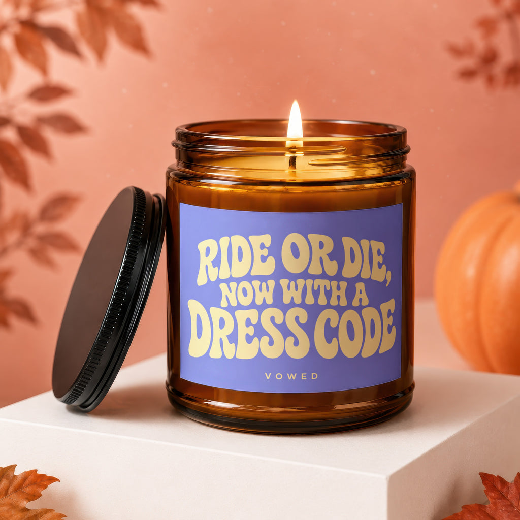 Amber candle with lit wick, purple label reading "RIDE OR DIE, NOW WITH A DRESS CODE" and "VOWED".