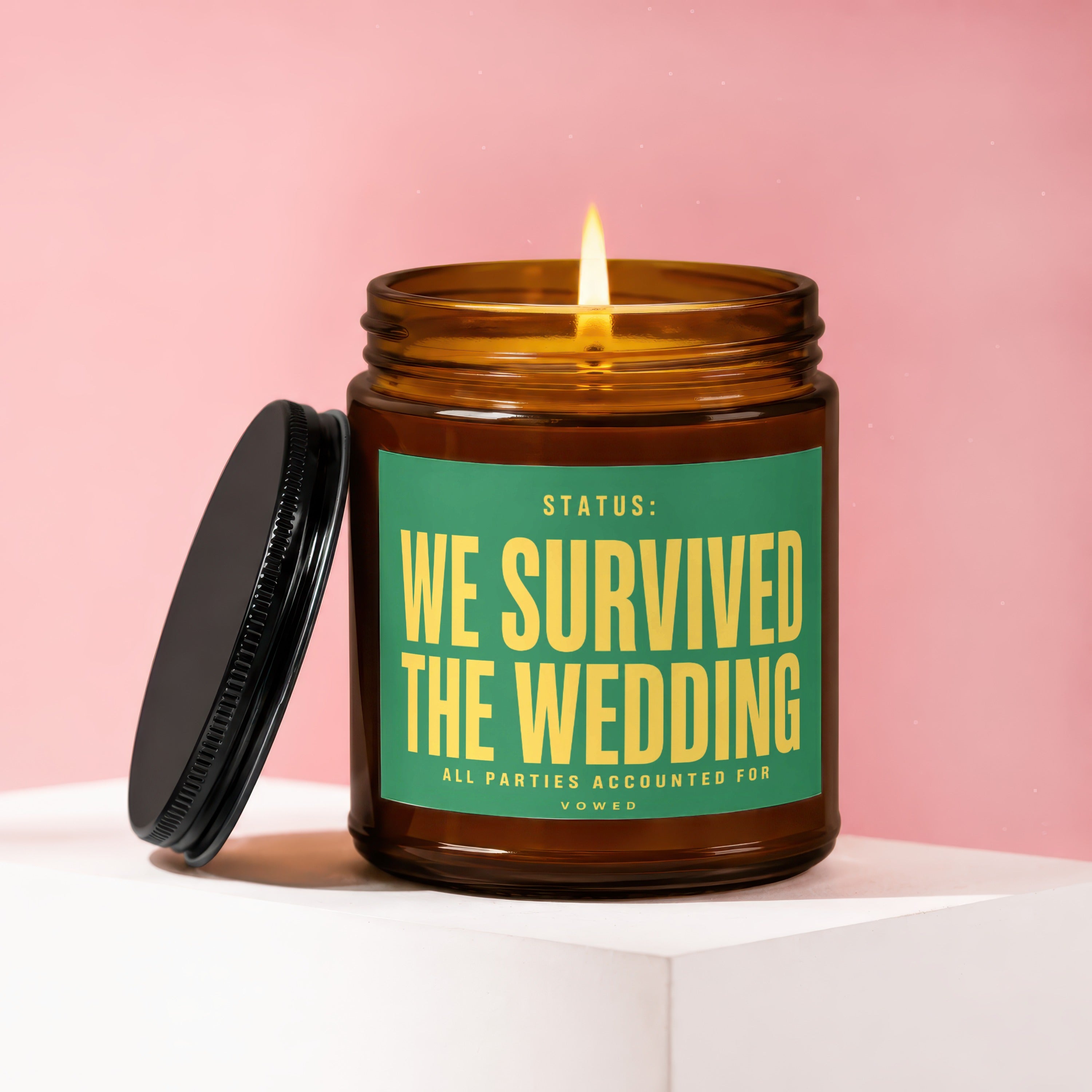 Amber glass candle with lit flame and "We Survived The Wedding" text.
