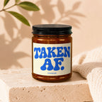 Amber glass candle with black lid and label reading "TAKEN AF. VOWED".