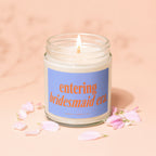 Glass jar candle with "entering bridesmaid era" text and pink petals on a peach background.