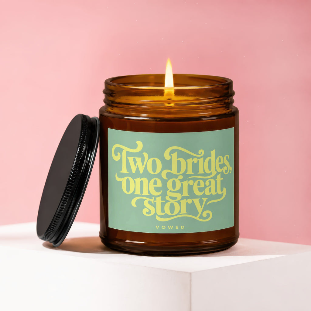 Amber jar candle with lit flame, lid detached. Text: "Two brides, one great story."
