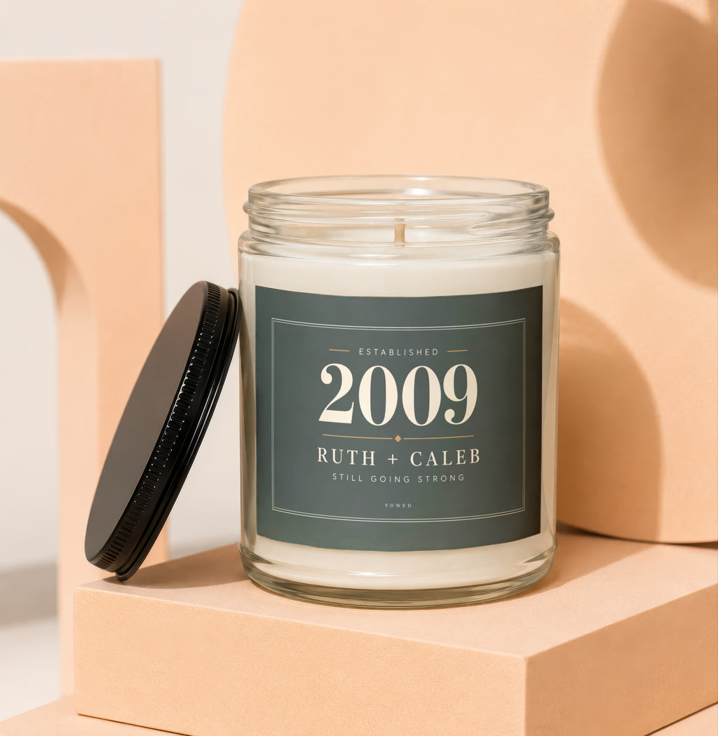 Glass candle with a dark green label reading "Established 2009 Ruth + Caleb Still Going Strong".