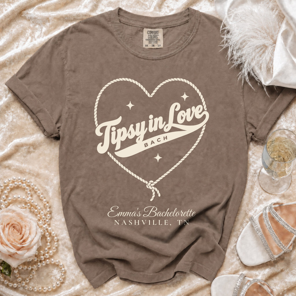 Brown t-shirt featuring a rope heart graphic, the text "Tipsy in Love BACH", and "Emma’s Bachelorette NASHVILLE, TN".