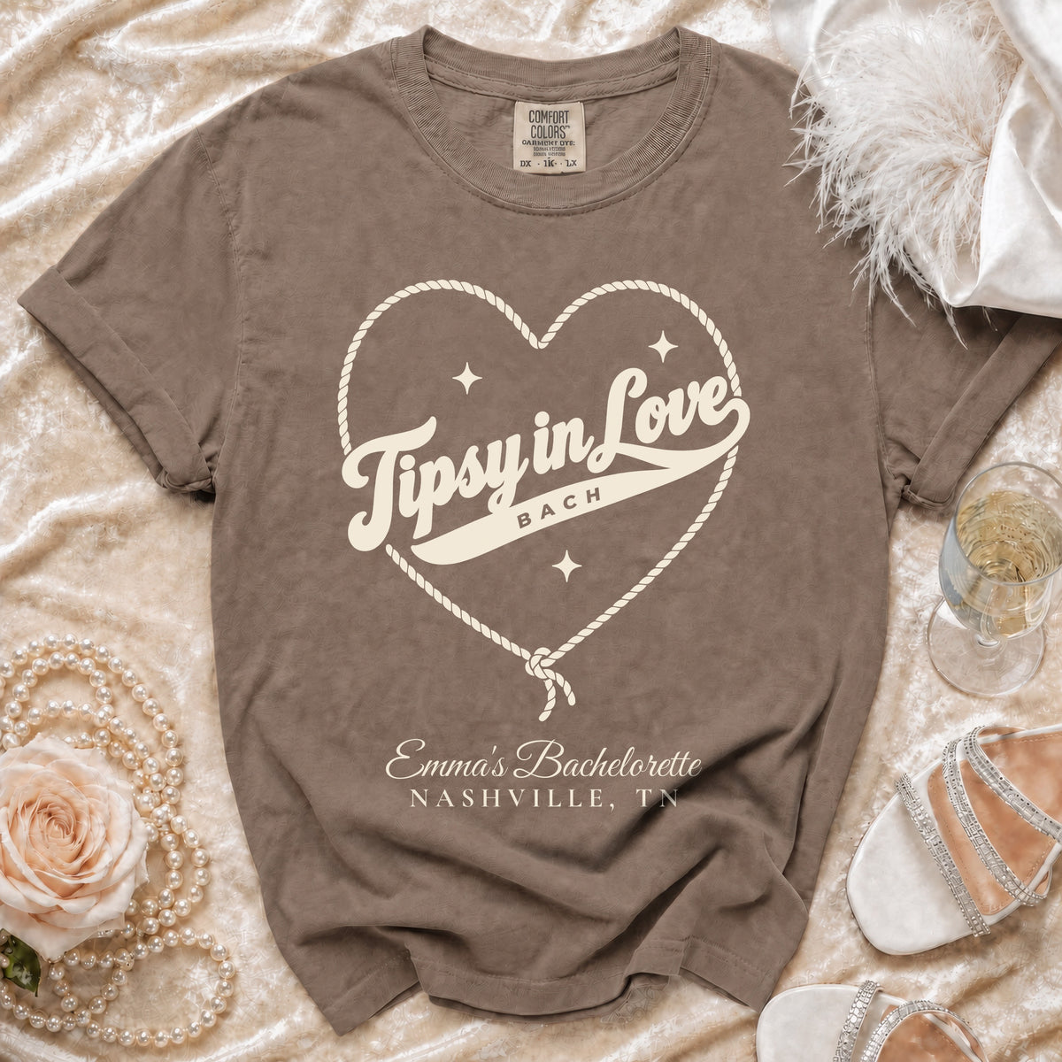 Brown t-shirt featuring a rope heart graphic, the text "Tipsy in Love BACH", and "Emma’s Bachelorette NASHVILLE, TN".