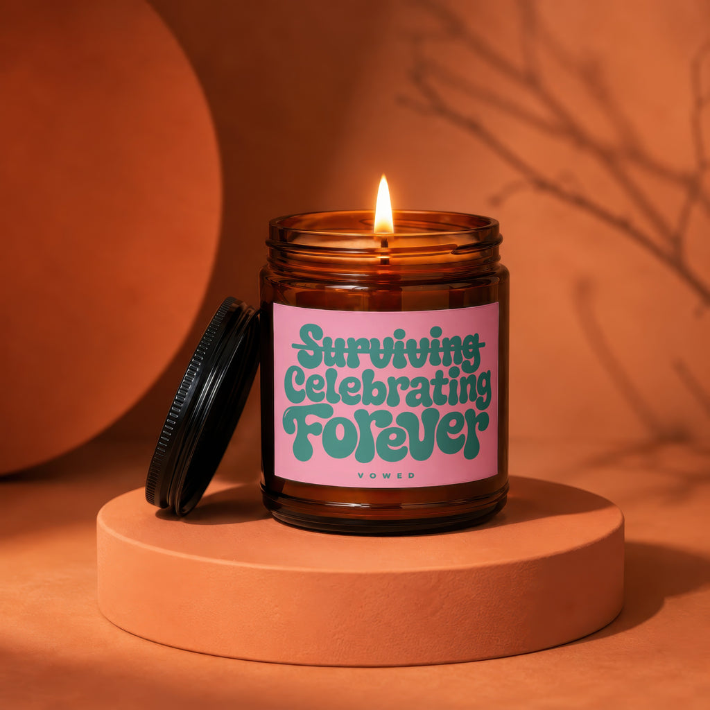 Amber jar candle with pink label reads "Surviving Celebrating Forever Vowed".