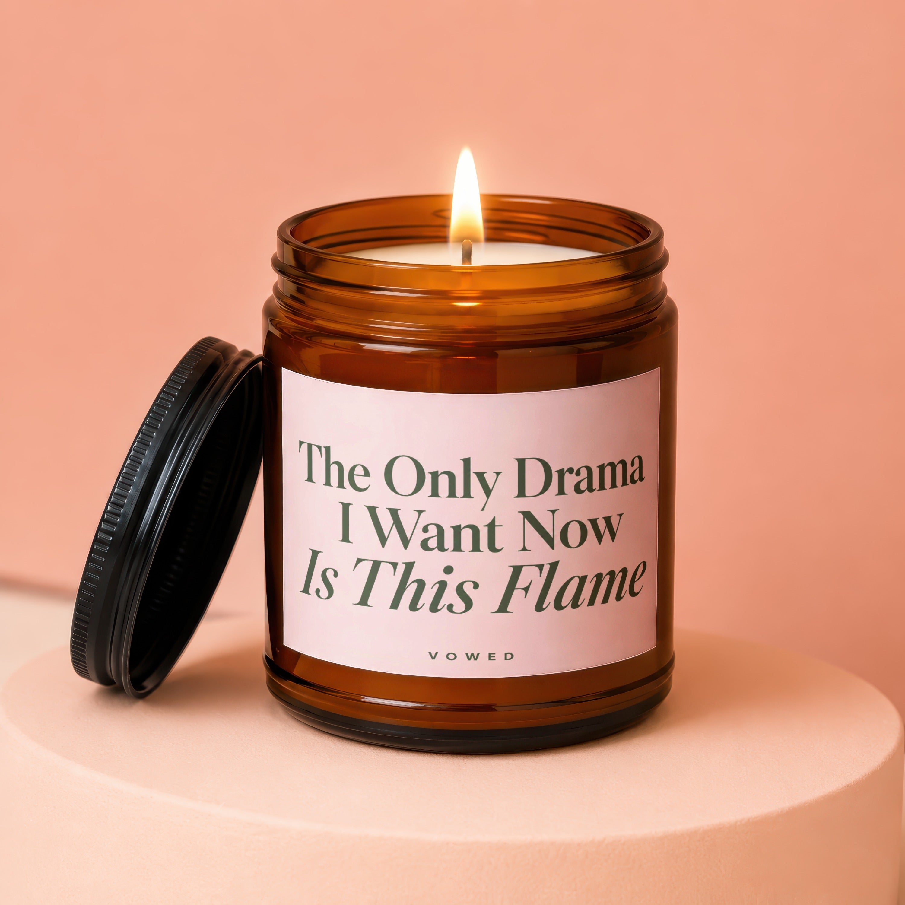 Amber glass candle with lid off, lit flame, and text "The Only Drama I Want Now Is This Flame".