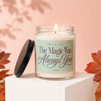 Candle labeled "The Magic Was Always You" with lid off, surrounded by autumn leaves.