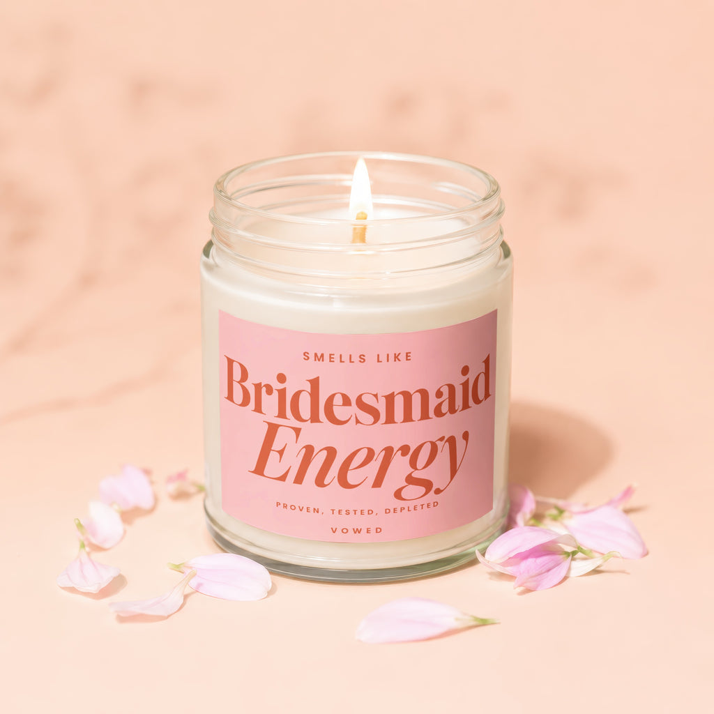 Glass jar candle with pink label reading "Smells Like Bridesmaid Energy Vowed".