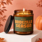 Burning candle in amber jar with "Bridezilla Season" text, near pumpkin and leaves.