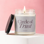 Lit candle in glass jar with label "Circle of Trust" on pink background.