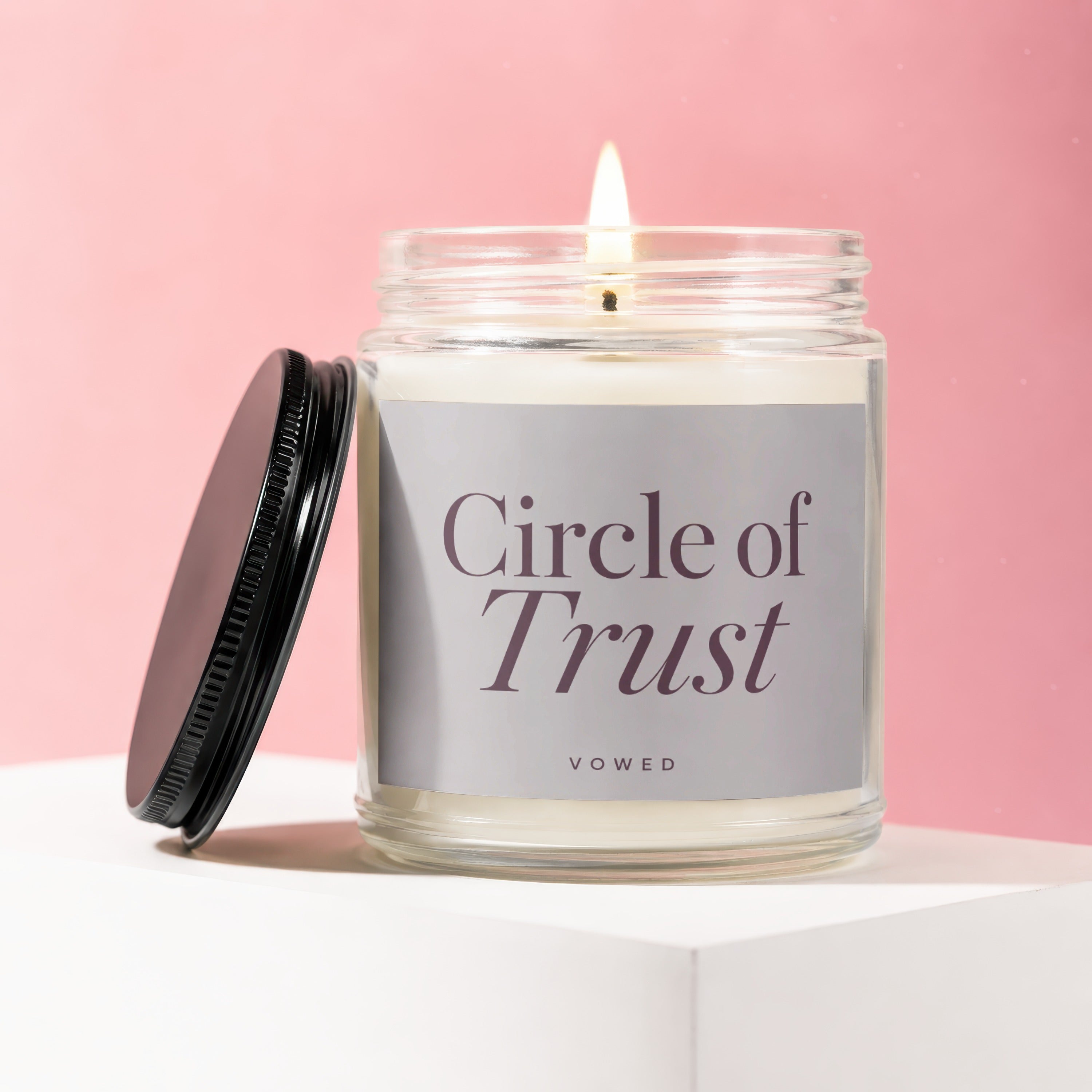 Lit candle in glass jar with label "Circle of Trust" on pink background.