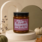 Amber candle with pink label that reads "Two husbands, one to-do list" and "VOWED".