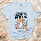 Light blue t-shirt with "Olivia's Bach Reckless in Texas Austin, TX Summer 2026" and Texas motifs.